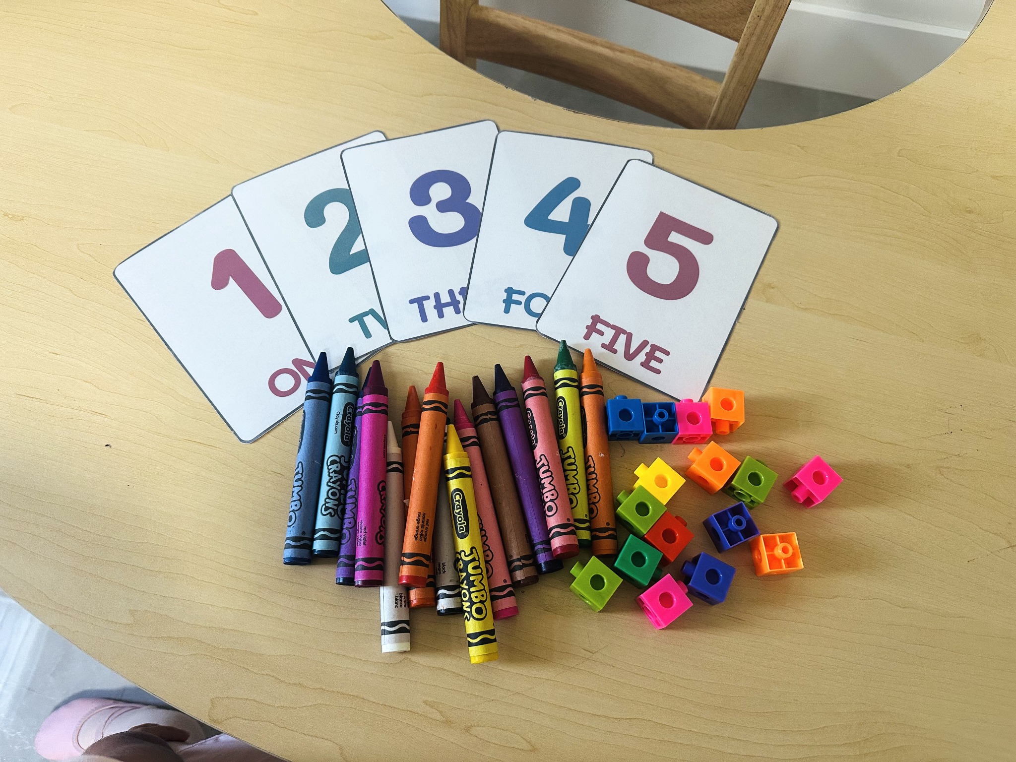 Number cards one through five, crayons, and colorful linking cubes on a wooden homeschool table